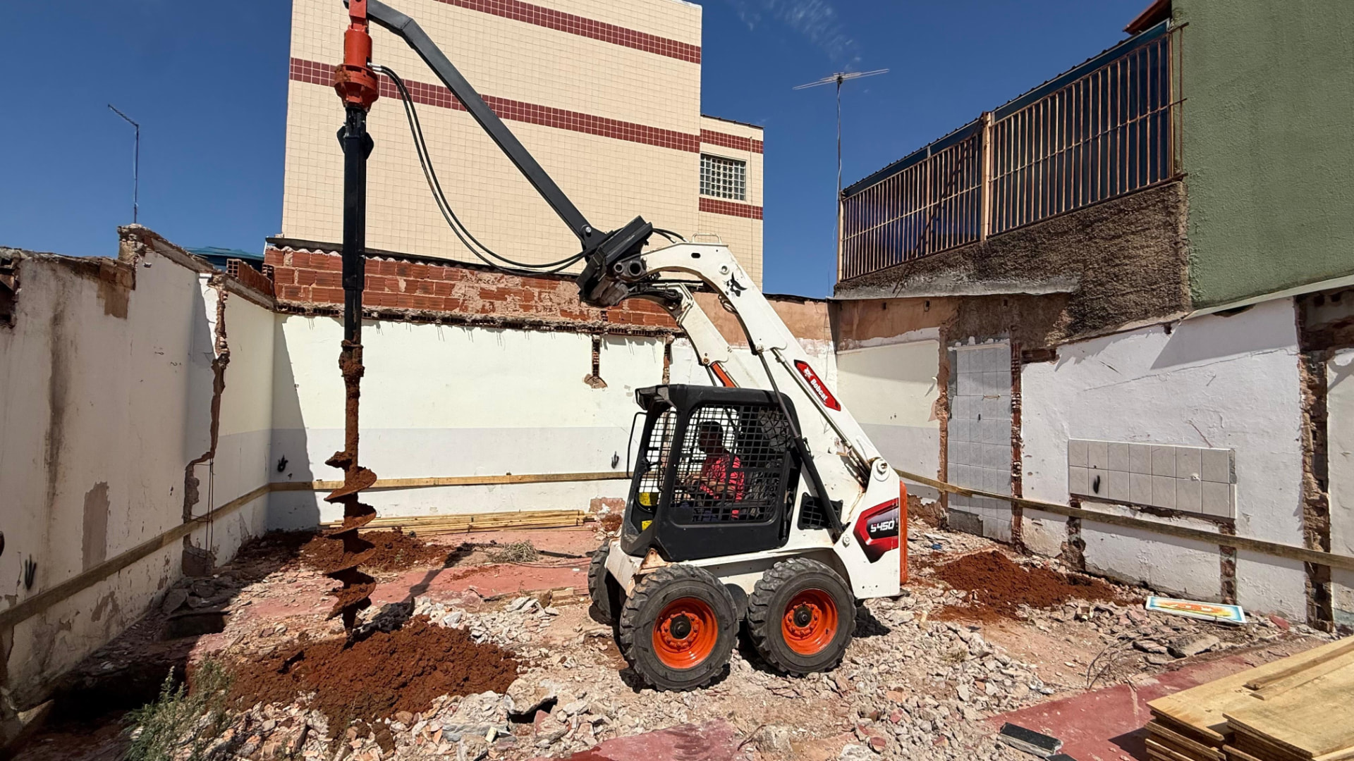 Bobcat da RM com perfurador de solo trabalhando em uma obra